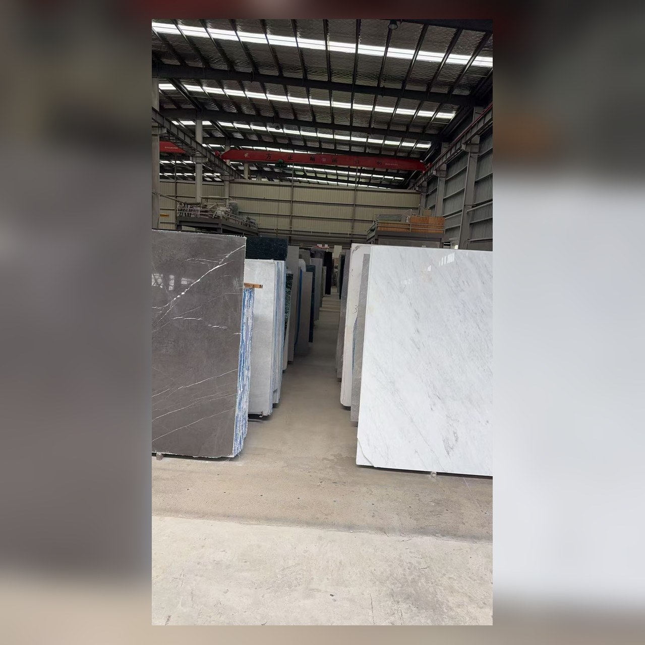 方正精品石材厂房大板仓库：白灰黑各色大理石大板整齐陈列，顶部方正精品石材行车